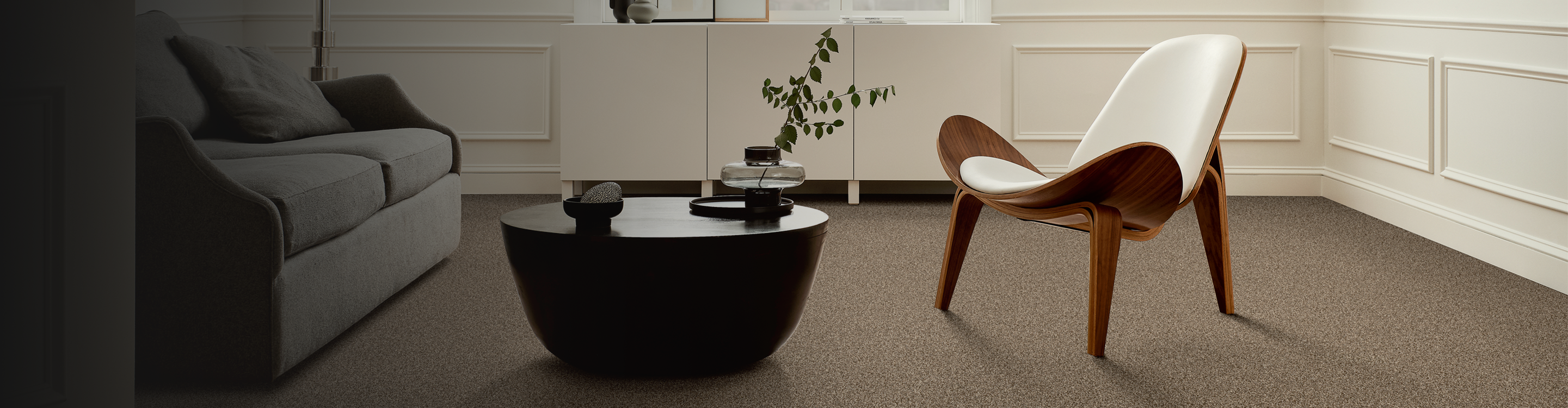 beige carpeted floors in contemporary modern living room with white chair, black coffee table and abstract art